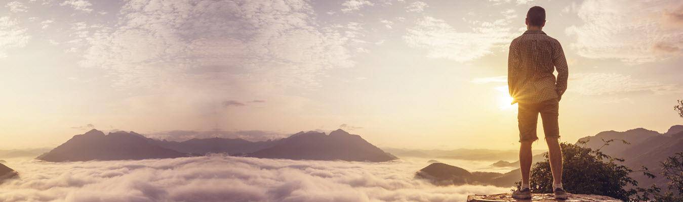 Man standing triumphantly on mountain peak, overlooking a stunning sunrise above the clouds.